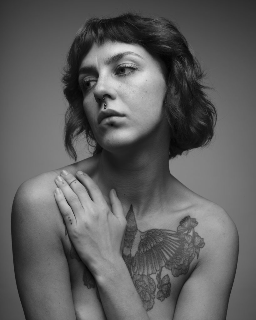 black and white portrait of a beautiful woman with a chest tattoo. BRIGHTON